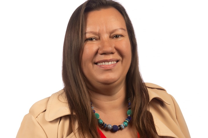 Celia Harnas smiles at the camera, wearing red shirt, brown jacket.