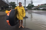George from Hermit Park stands with an inflatable raft and wearing yellow raincoat in flooded Townsville.