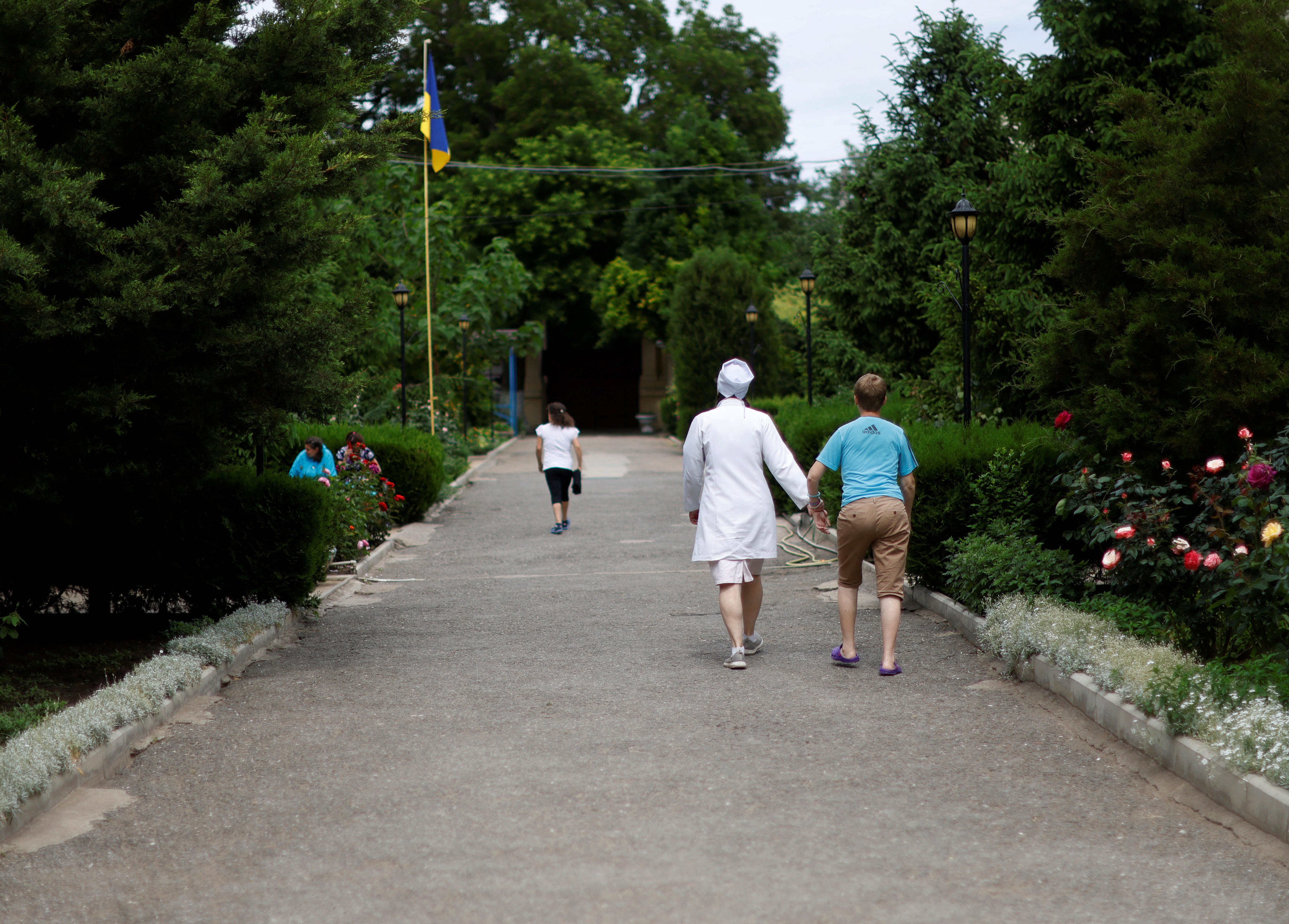 woman walks with child through a garden holding their hand. 