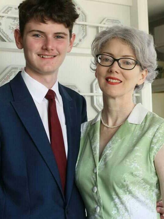 A teenage boy in a shirt and tie with his mother in pearls both smiling