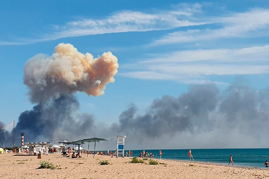 Rising smoke can be seen from the beach, while beachgoers mill around.
