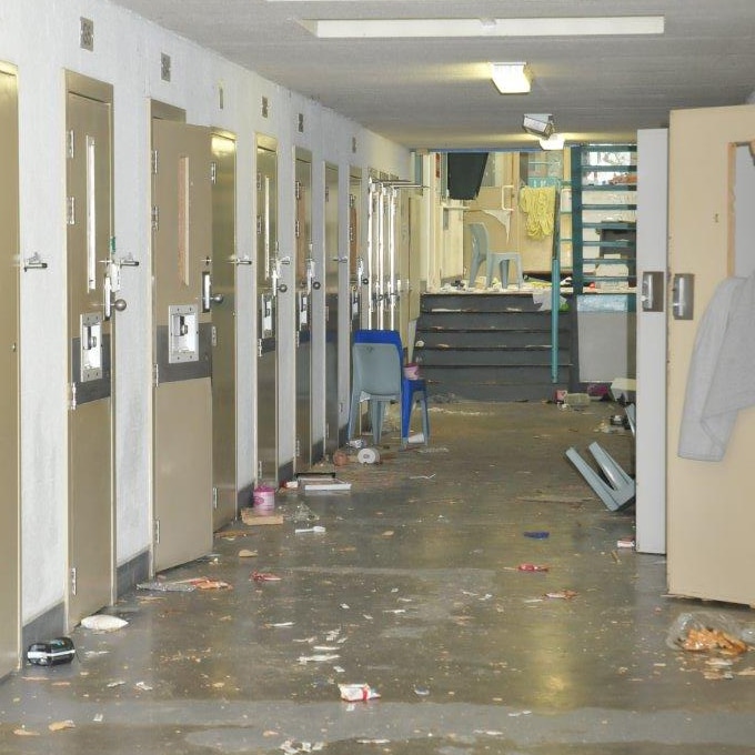 Cell doors lie ajar and debris is scattered around a damaged corridor at Greenough Regional Prison.