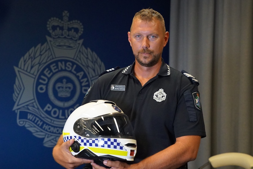 a police officer holds a branded motorbike helmet standing in front of a wall with a police badge painted on it