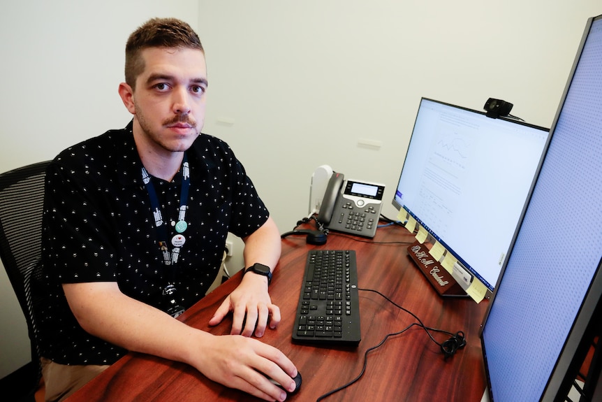 a young man with a moustache working at a computer in an office