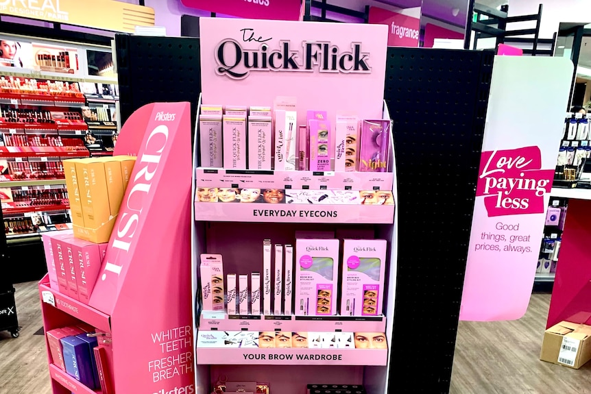 A tall, thin pink display stand with a variety of cosmetic products for sale.