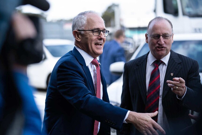 A smiling Malcolm Turnbull extends a handshake to someone unseen in the photo.