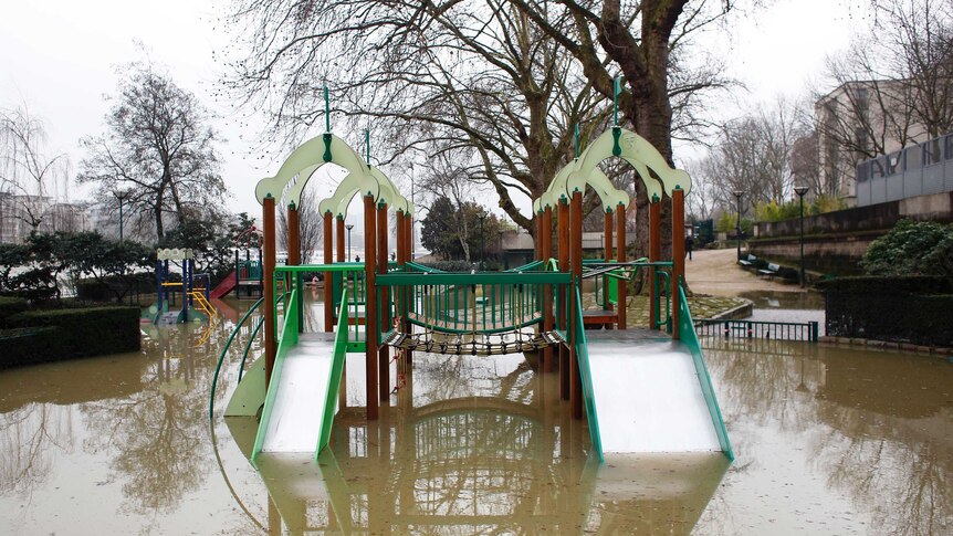 flood waters have risen up past a playground, with the water level sitting at the middle of the slippery dip.