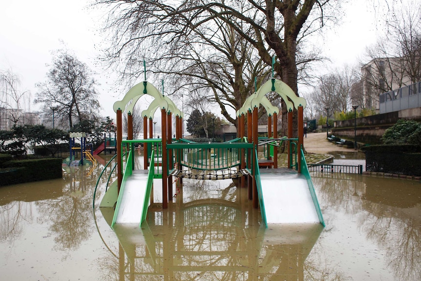 flood waters have risen up past a playground, with the water level sitting at the middle of the slippery dip.