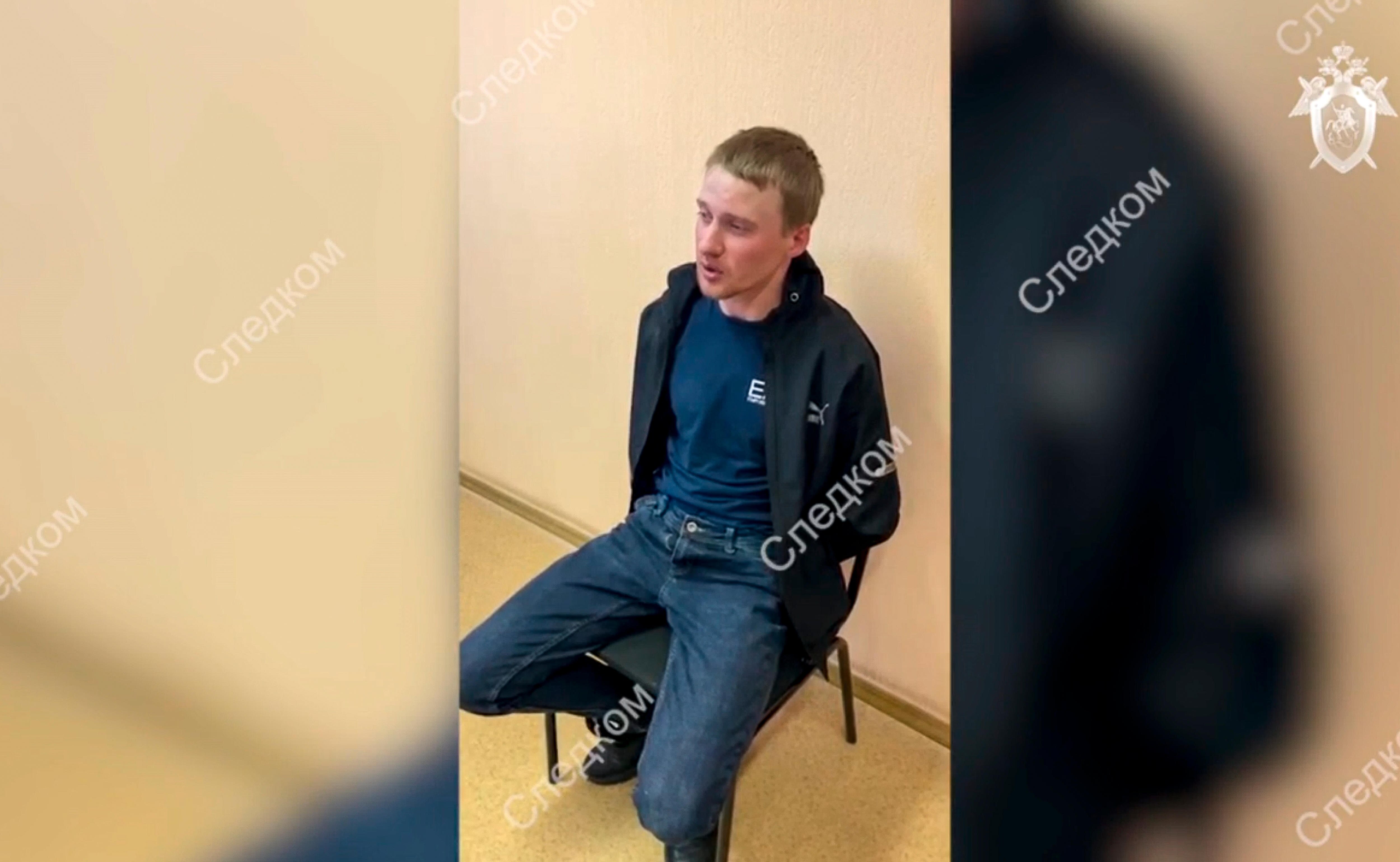 A detained suspect sits in a police station in a video still marked with Russian writing.