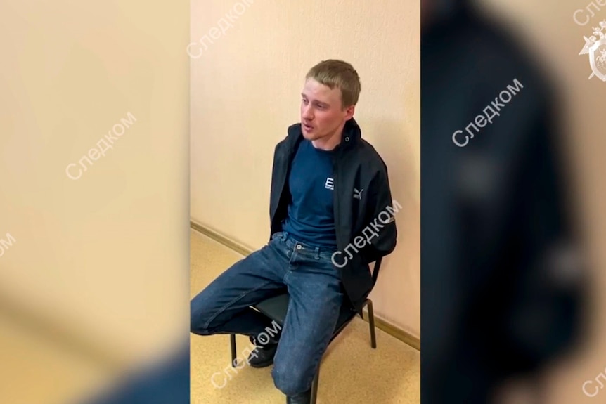 A detained suspect sits in a police station in a video still marked with Russian writing.