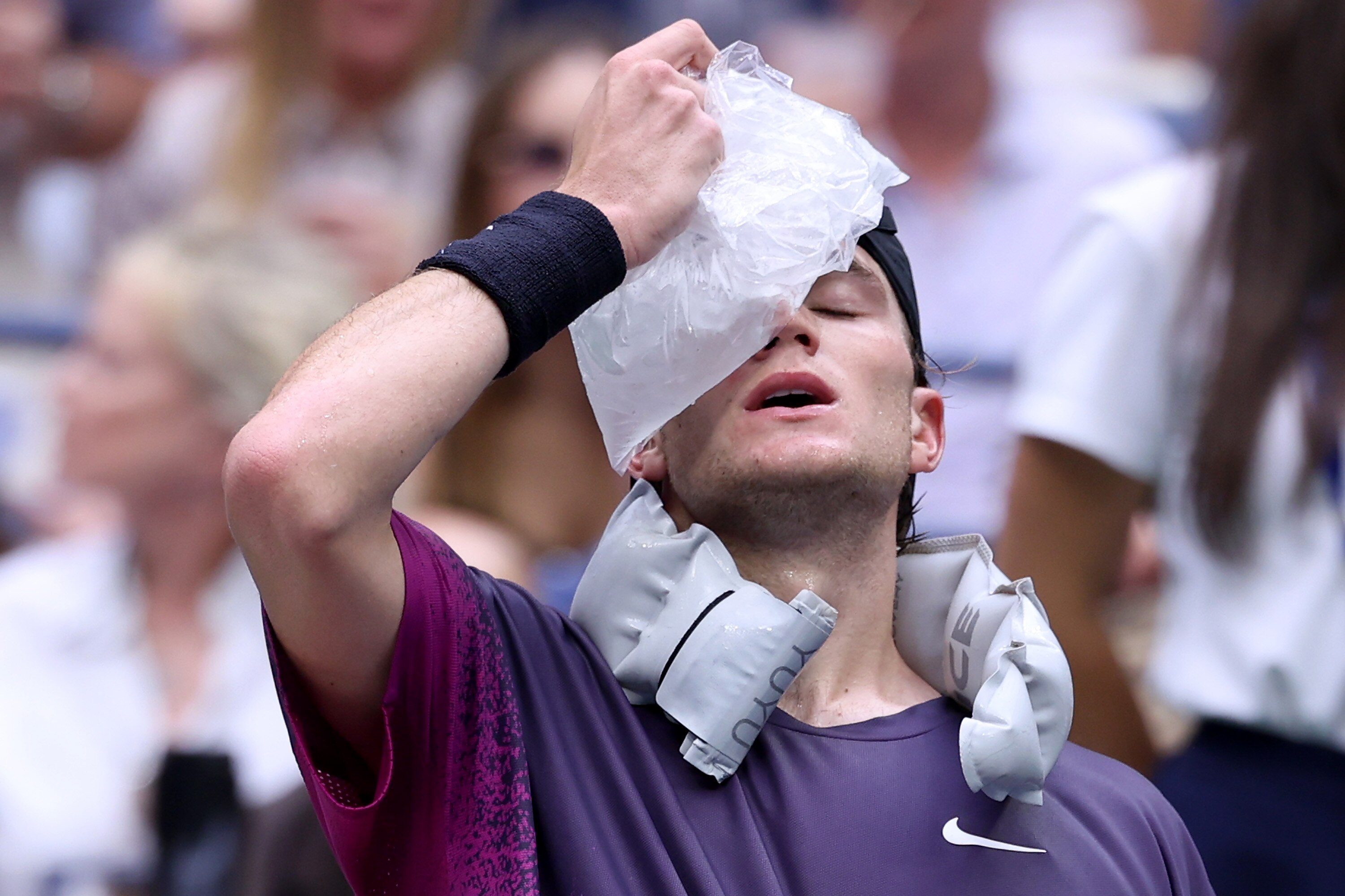 British tennis player Jack Draper sits at courtside breathing heavily with his eyes closed as he holds an icepack to his face.
