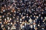 A group of Japanese people walking through a crowd with many wearing face masks