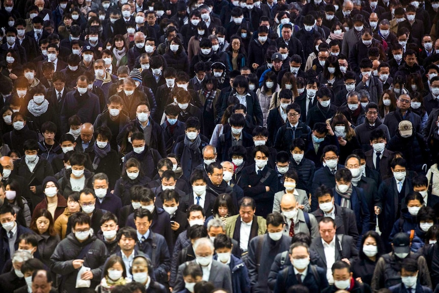 A group of Japanese people walking through a crowd with many wearing face masks