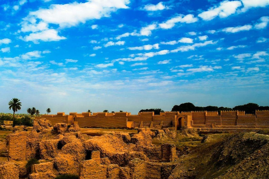 Under a blue, slightly cloudy sky sit large boulders and, behind them, orange brick walls.