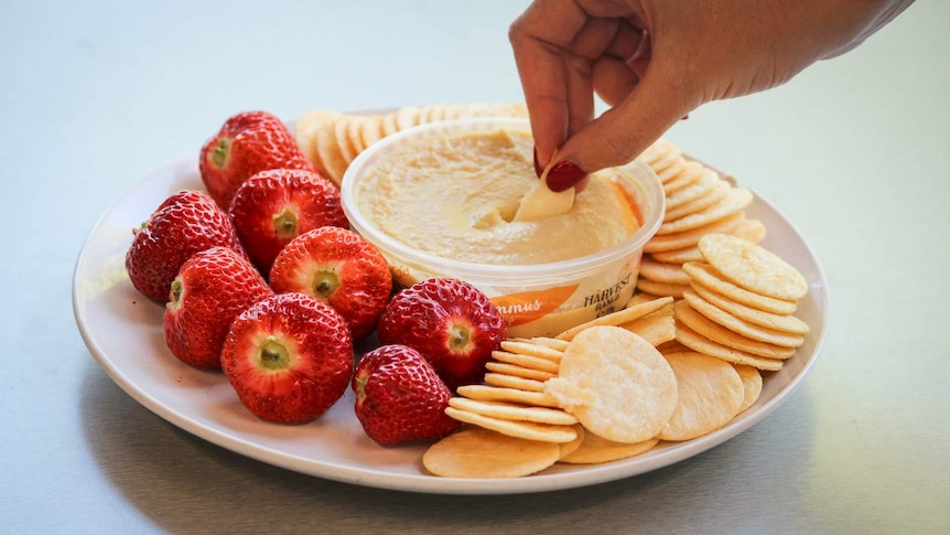 A woman dips a cracker into a bowl of dip.