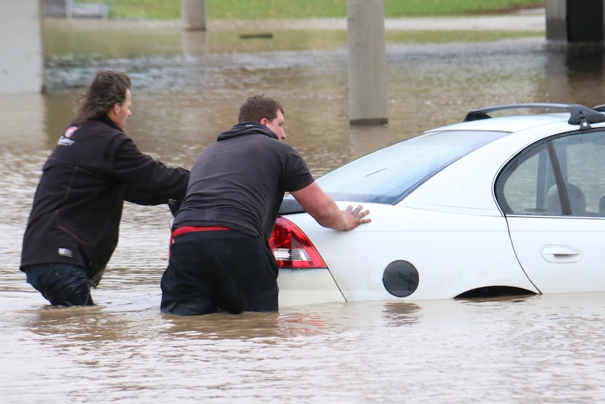 Two push a  white car through deep floodwaters
