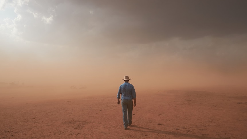 Art photograph of a farmer walking towards a red dust storm over drought parched land