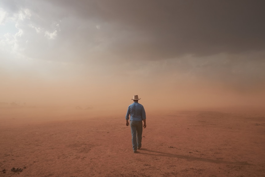 Fotografía artística de un agricultor caminando hacia una tormenta de polvo rojo sobre tierras resecas por la sequía