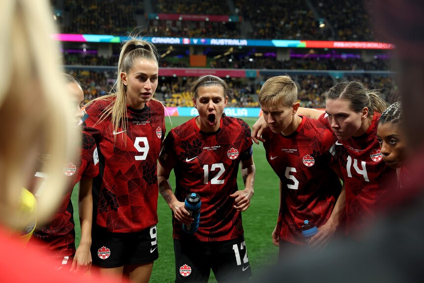 A group of women soccer players wearing red, black and white stand in a huddle before a big game