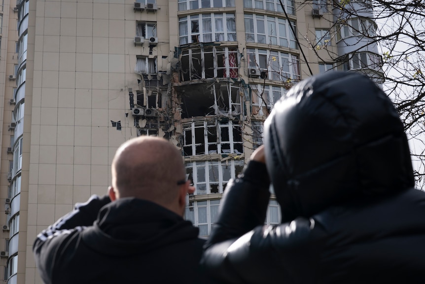 People look at an apartment building damaged by a drone that was shot down, during a Russian overnight strike.