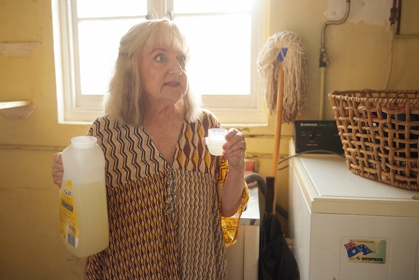 A woman holds a bottle of washing dtergent in a laundry.