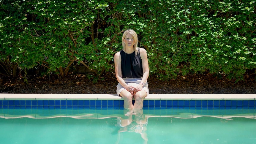 Julie Gilbert sits on the edge of her pool with her legs in the water.