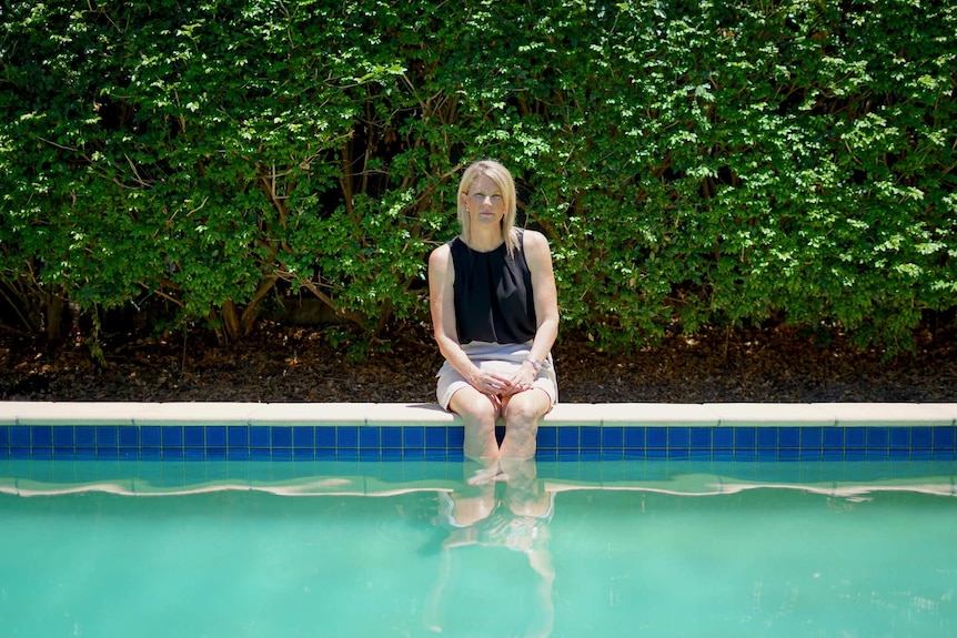 Julie Gilbert sits on the edge of her pool with her legs in the water.