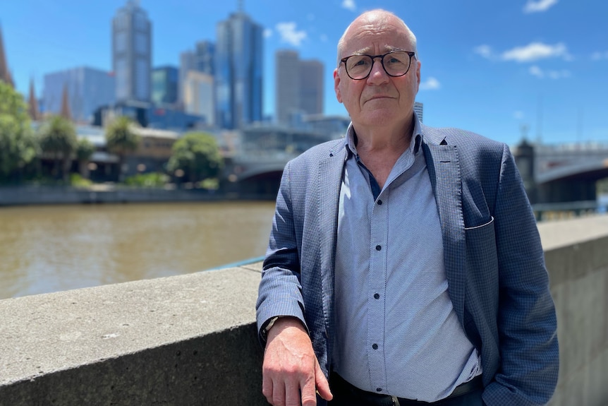 Judge Michael Bourke leans on a concrete fence with the Yarra River and Melbourne's CBD behind him. 