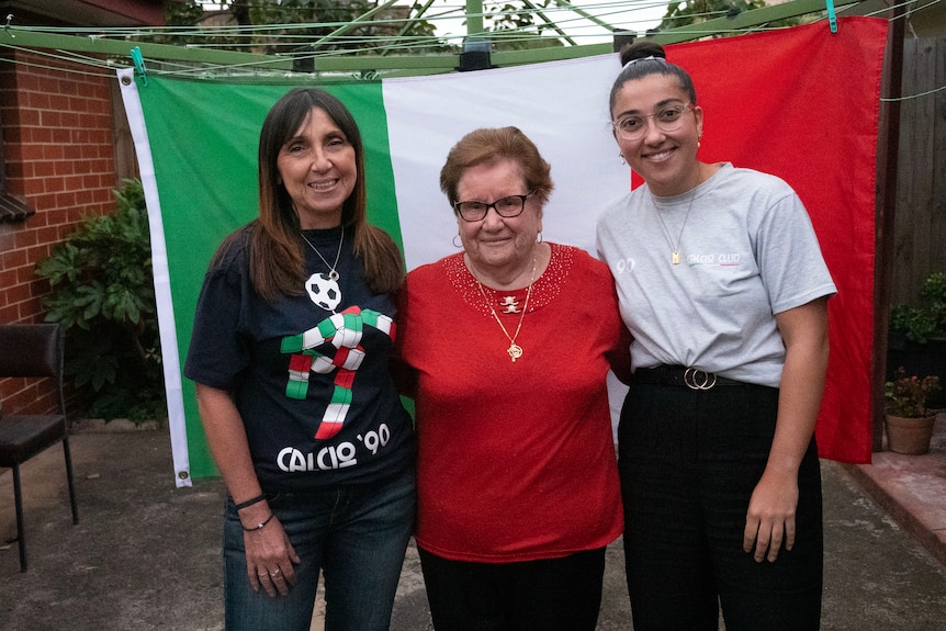 A closeup of the three Italian supporters, wearing a red, blue and grey shirts, and an Italian flag held behind them.