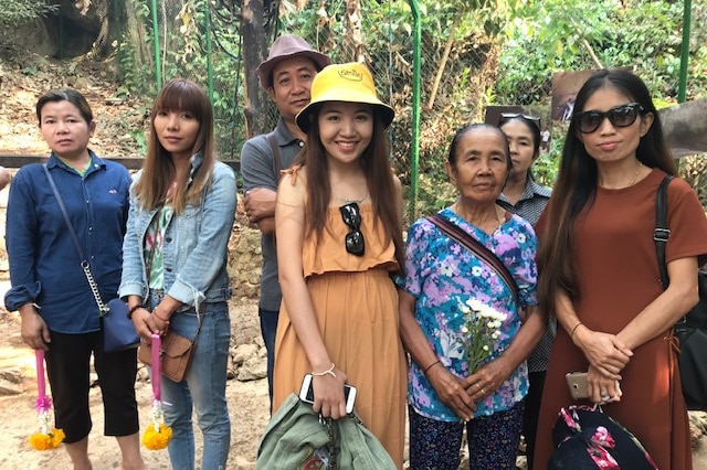 A group of men and women standing outside the Tham Luang cave, smiling into the camera