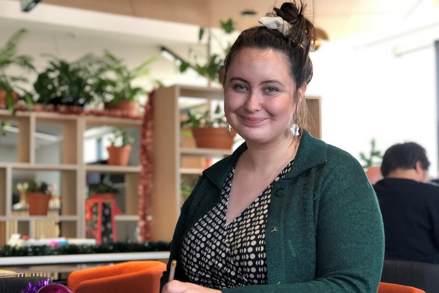 Rebecca Egan smiles as she writes a Christmas card, dressed in a green cardigan.