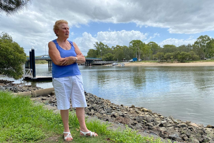 An elderly woman stands along a beach at a canal