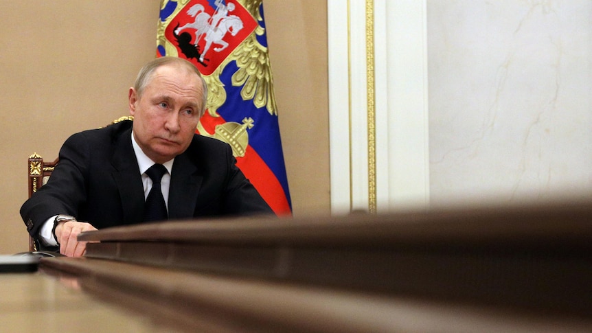 A low angle photo of Vladimir Putin listening at a conference table