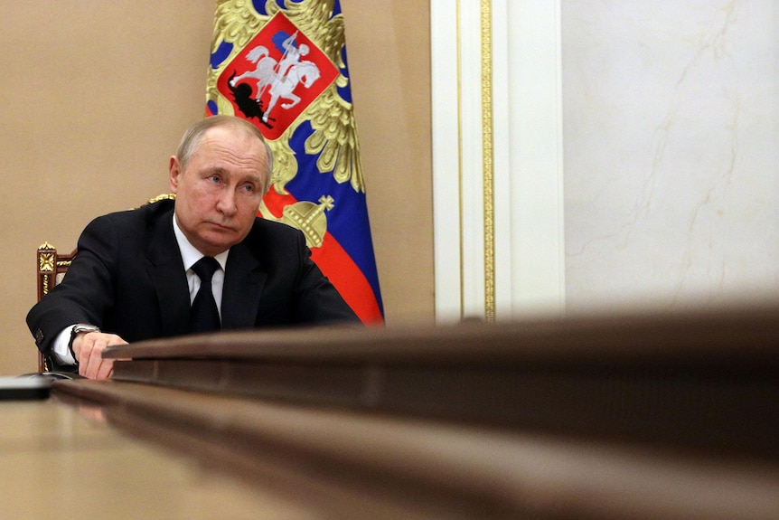 A low angle photo of Vladimir Putin listening at a conference table