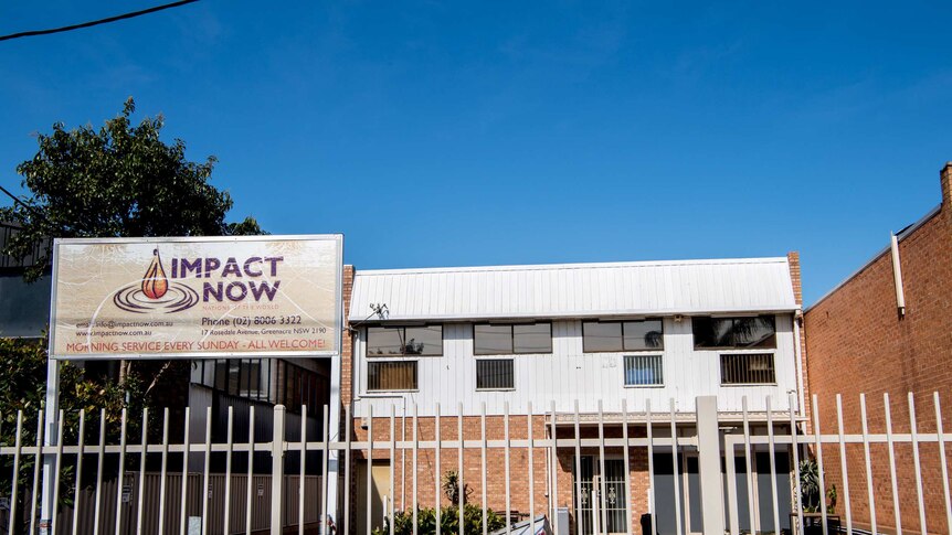 An industrial looking site sits behind a sign that says 'Impact Now service every Sunday, all welcome'