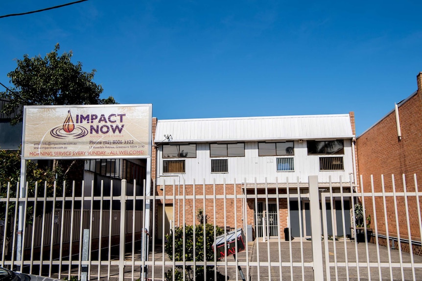 An industrial looking site sits behind a sign that says 'Impact Now service every Sunday, all welcome'