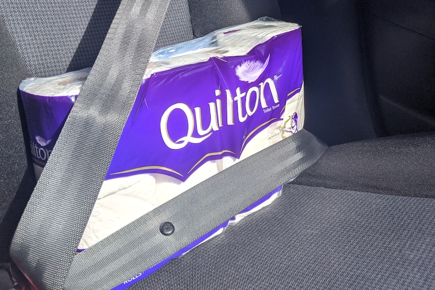 A packet of toilet paper restrained by a seat belt in the back seat of a car