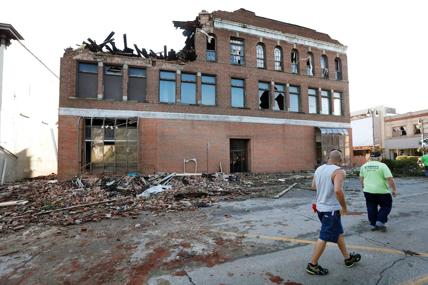 Residents walk past a tornado damaged brick building