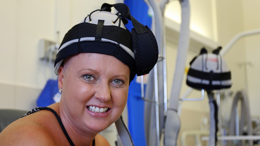 Jodie McRae wears a cap attached to a scalp cooling machine