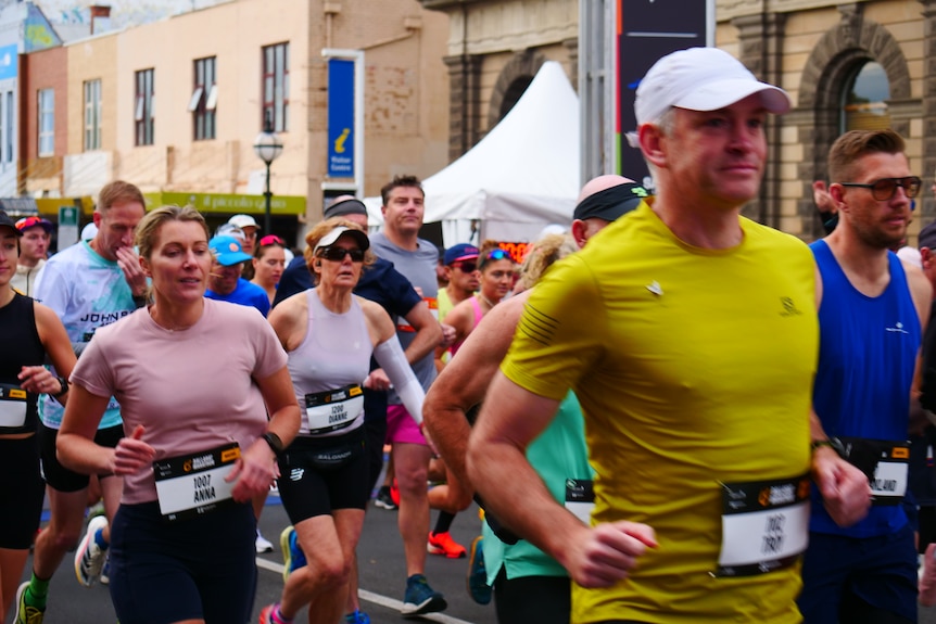 Runners smile as they run in a pack along a busy street.