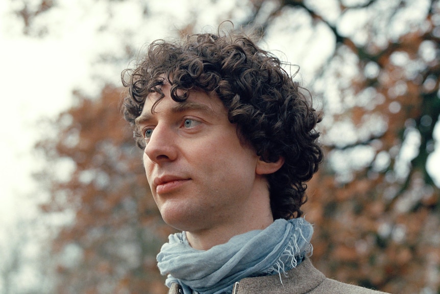 Portrait of young Caucasian man with brown short curly hair wearing a scarf in Autumn in the UK. 