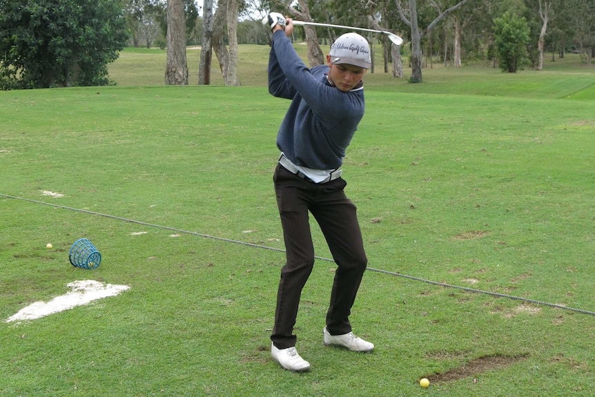 A teenager takes a back swing at a golf driving range.