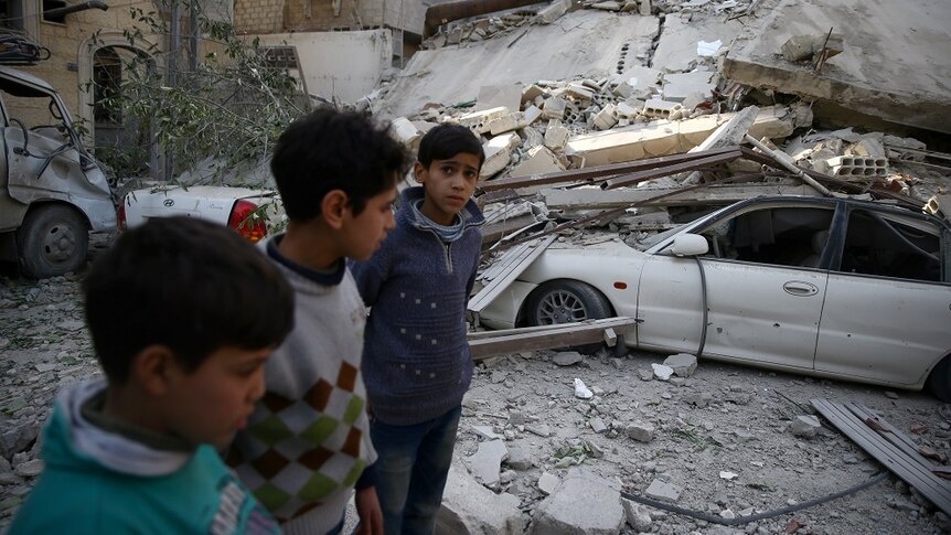 Three young boys look concerned as they walk amid rubble.