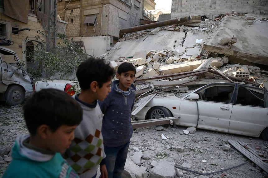 Three young boys look concerned as they walk amid rubble.