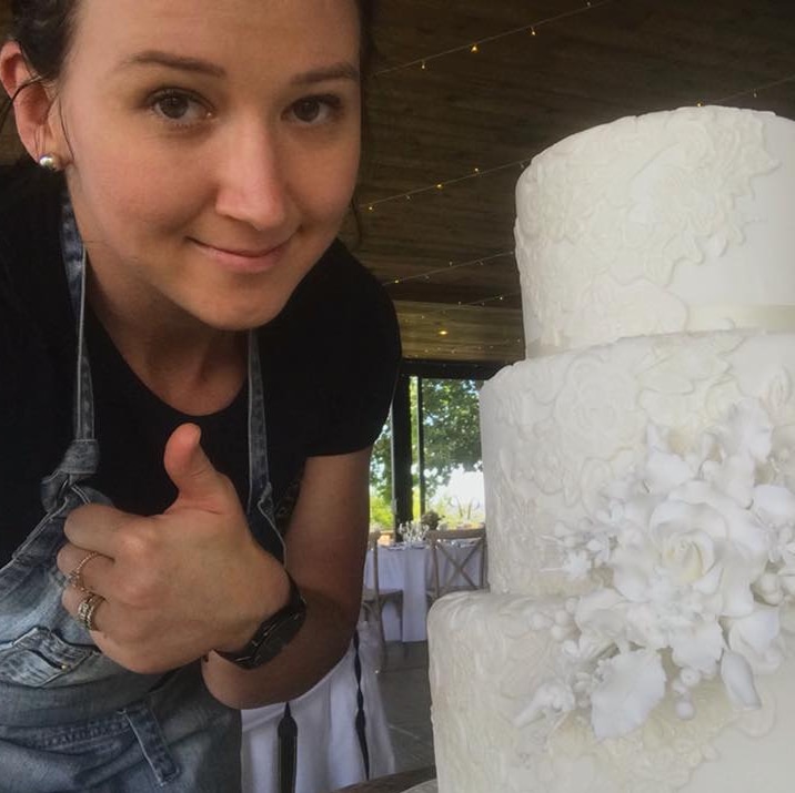 A woman taking a selfie with a white wedding cake.
