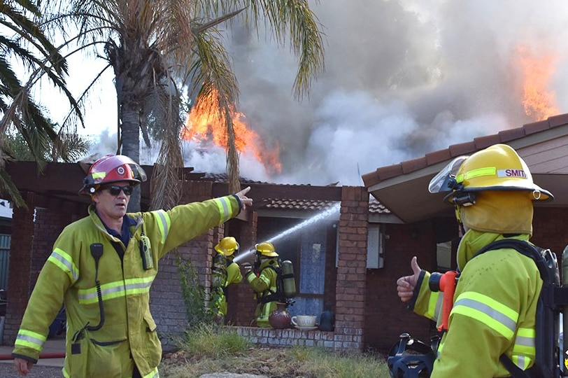 Two fire fighters discussing the house fire that they are standing in front of.