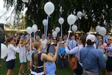 Dozens of people and children wearing blue release white balloons.