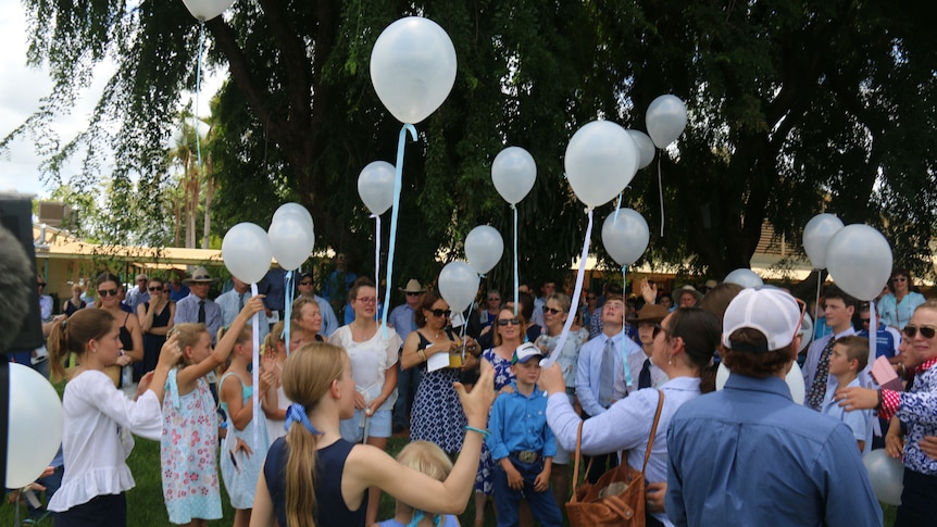 Dozens of people and children wearing blue release white balloons.