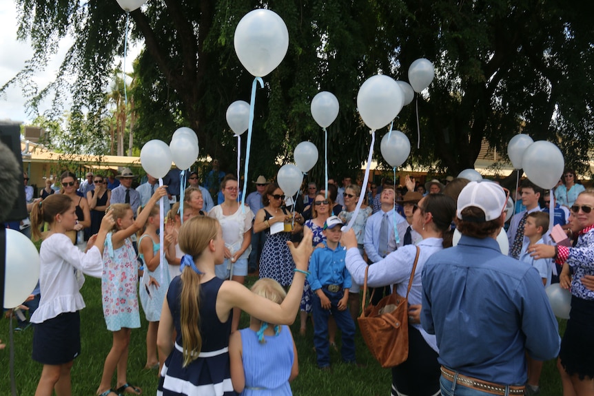 Dozens of people and children wearing blue release white balloons.