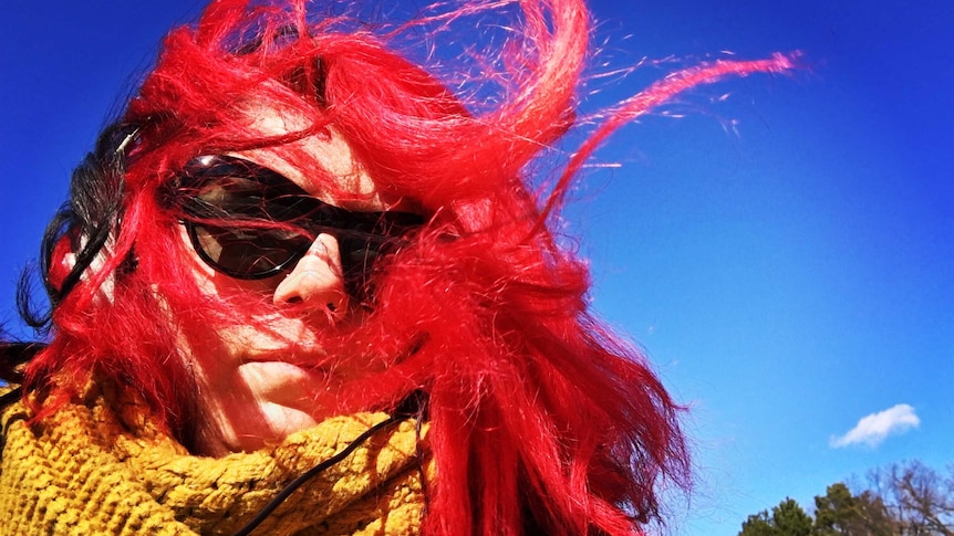 A woman's bright red hair blows around in windy weather.